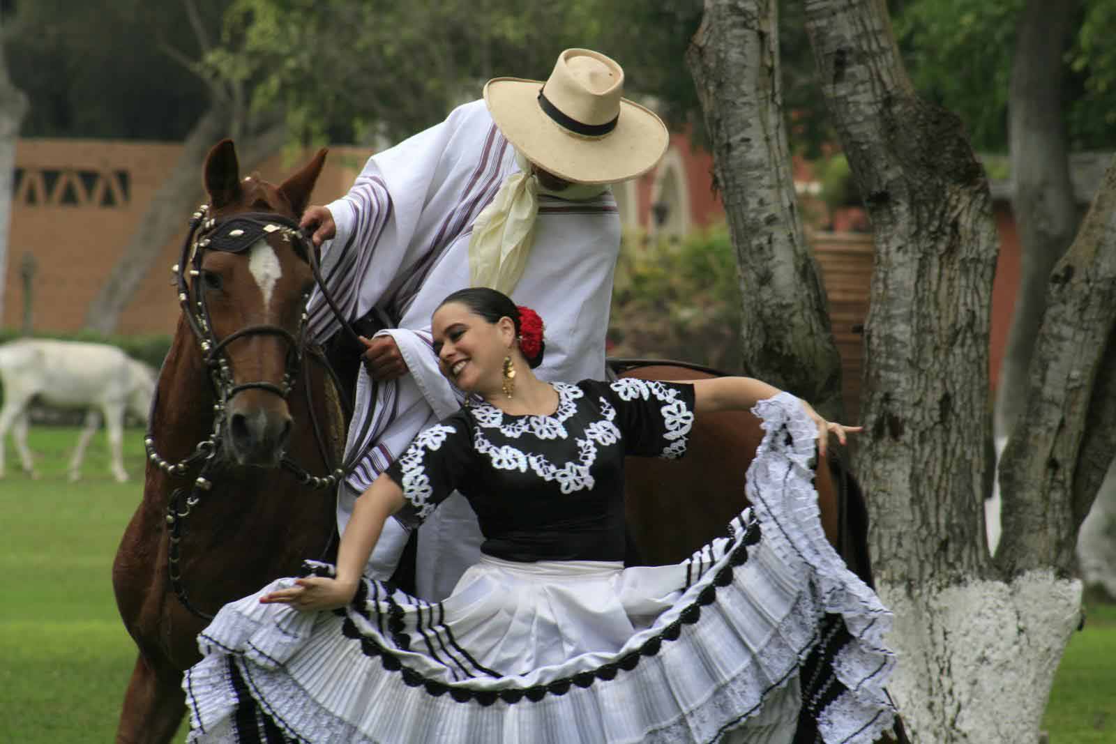 Bailarina de marinera con vestido blanco y negro junto a un chalán a caballo de paso peruano