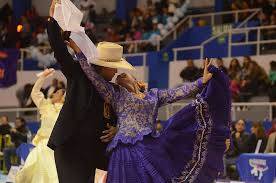 Bailarina con falda morada en vuelo y su pareja con sombrero durante un concurso en un pabellón deportivo