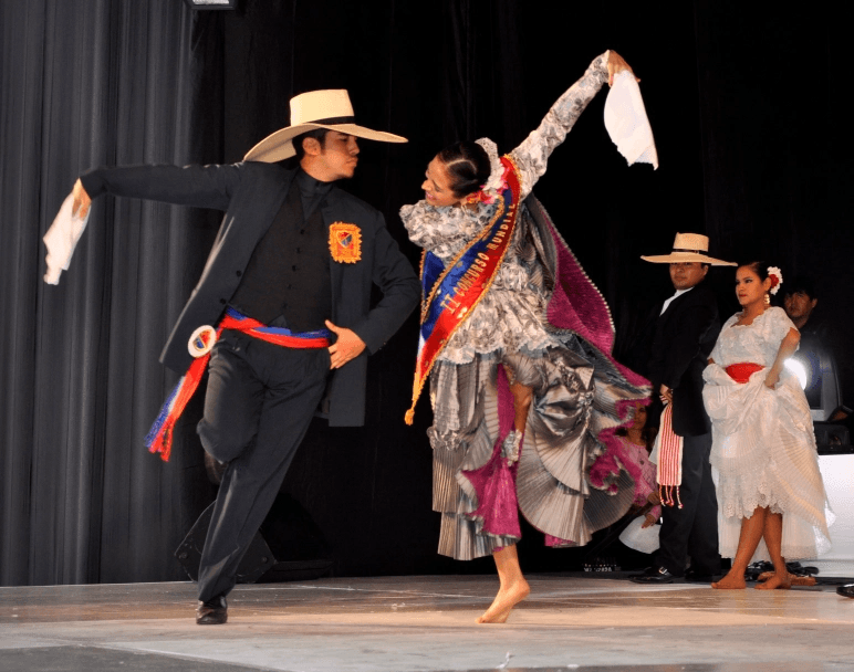 Bailarín con traje negro y sombrero alza el pañuelo junto a su pareja en un ensayo sobre el escenario