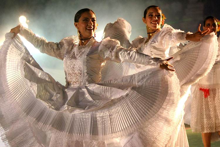 Dos bailarinas con vestidos blancos de encaje abren sus faldas en un escenario iluminado durante la Fiesta del Perol