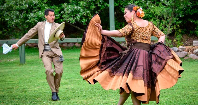 Pareja ensayando marinera en un jardín: ella con falda marrón en vuelo y él con sombrero de paja