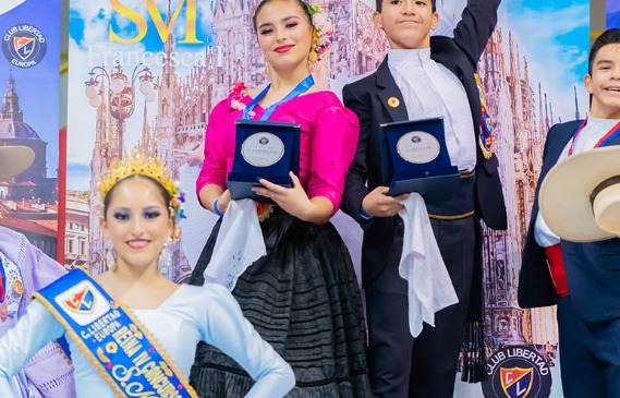 Pareja junior mostrando sus medallas del IV Concurso Europeo Milán 2022, ella con vestido negro y flores en el pelo