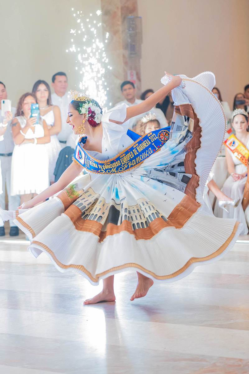 Reina de marinera con banda y vestido blanco bordado haciendo girar la falda durante una presentación