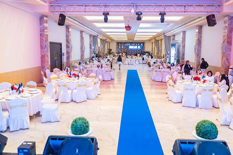Salón de eventos con mesas vestidas de blanco y alfombra azul central preparado para la Fiesta del Perol